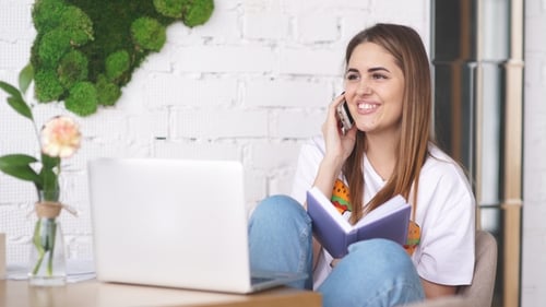 una joven autónoma con un cuaderno y una computadora portátil trabaja en un café.