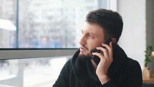 a Young Businessman Talking on the Phone and Working at a Laptop in a Cafe