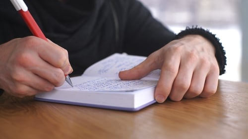 Person Writing in Notebook with Red Pen