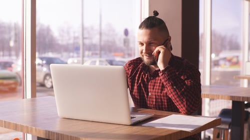 Young Businessman Talking on the Phone and Working at a Laptop in a Cafe
