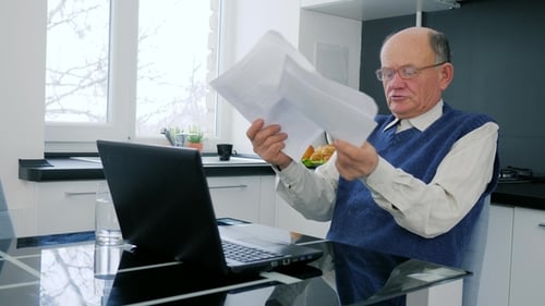 Senior Man Looks Concerned With Laptop and Papers