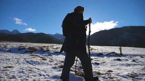 Young Hiker Going Nordic Walking with Sticks on Snowy Trail in Field with Sunlight at Background
