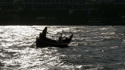 Silhouette eines kleinen hölzernen Fischerbootes mit Fischern, die sich am Meer bewegen Thailand Asien
