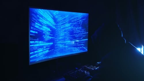 A Man Hacker in a Hood in a Dark Room Works with the Program Code