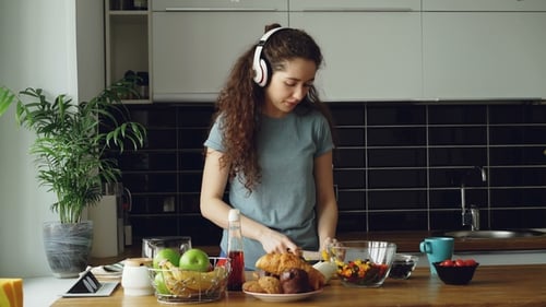 Woman Preparing Food in Bright Kitchen with Headphones