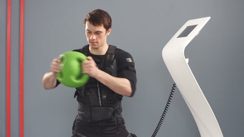 Young Man Exercises with EMS Suit and Ball