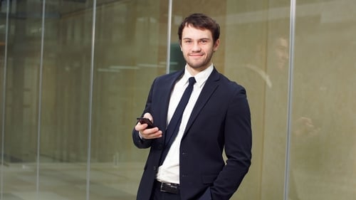Handsome Young Man Smiling at Smartphone in Office