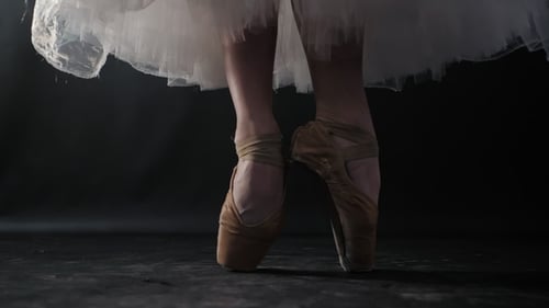 of Ballet Dancer As She Practices Exercises on Dark Stage or Studio. Woman's Feet in Pointe Shoes
