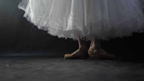 of Ballet Dancer As She Practices Exercises on Dark Stage or Studio. Woman's Feet in Pointe Shoes