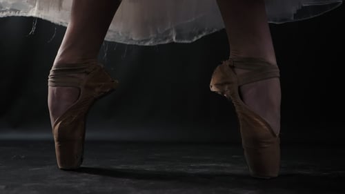 of Ballet Dancer As She Practices Exercises on Dark Stage or Studio. Woman's Feet in Pointe Shoes