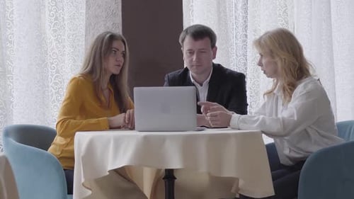 Three Serious Caucasian Business People Sitting at the Table with Laptop and Talking. Professional