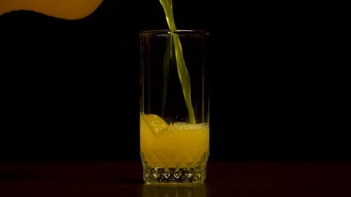 Orange Liquid Being Poured into Glass on Table