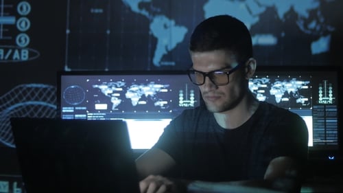 young Programmer Working at a Computer in the Data Center Filled with Display Screens