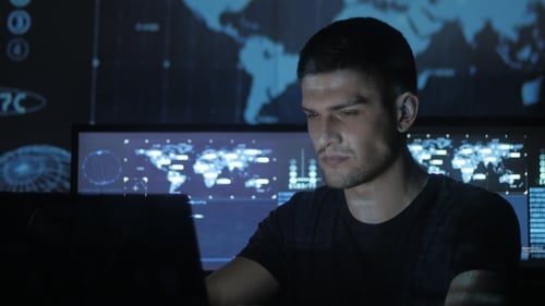 Portrait of a Young Programmer Working at a Computer in the Data Center Filled with Display Screens