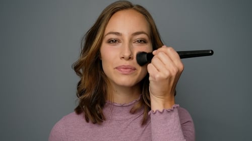 Woman Applies Makeup with Brush in Close Up