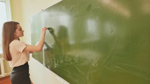 Young Woman Writing on Chalkboard in Classroom