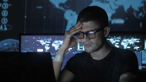 Portrait of a Young Programmer Working at a Computer in the Data Center Filled with Display Screens