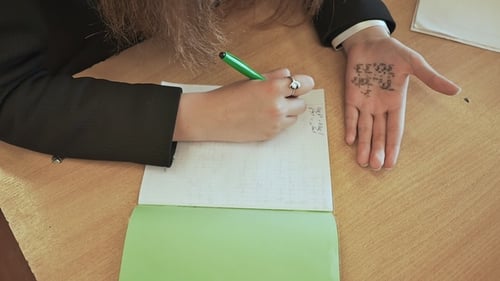 Das Schulmädchen schreibt mathematische Formeln aus einer Krippe an einer Hand ab. Schulprüfung.