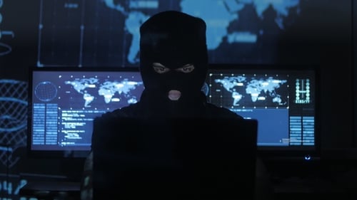 Masked man hacking on computer with code
