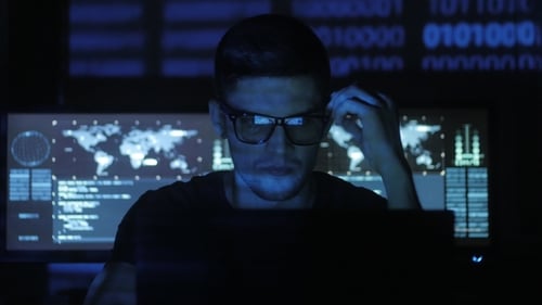 Hacker Programmer in Glasses Is Working on Computer While Blue Binary Code Characters Reflect on His