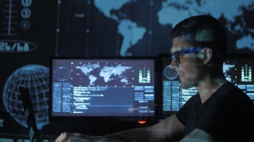 Portrait of a Young Programmer Working at a Computer in the Data Center Filled with Display Screens