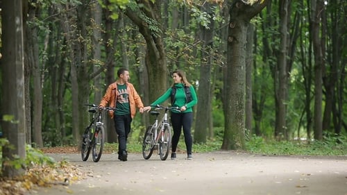 Man and Woman Walk Bikes in Park