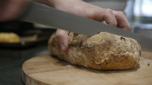 Loaf of Bread Being Cut on Wood Board