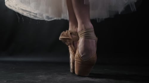 of Ballet Dancer As She Practices Exercises on Dark Stage or Studio. Woman's Feet in Pointe Shoes