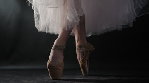 of Ballet Dancer As She Practices Exercises on Dark Stage or Studio. Woman's Feet in Pointe Shoes