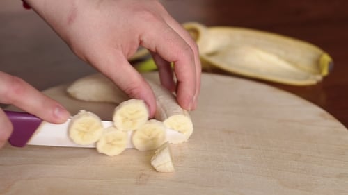 Hands Cutting a Banana on Cutting Board