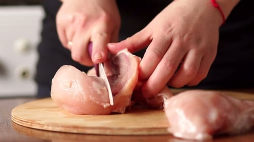 Chef de main féminine coupant la poitrine de poulet crue