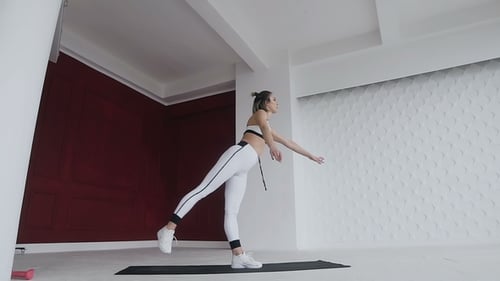 Frau in weißer Sportbekleidung stehend auf einem Bein, Yogapraxis drinnen