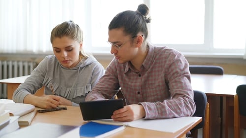 Jeunes étudiants travaillant ensemble à l'aide d'une tablette et discutant d'un projet de préparation aux examens