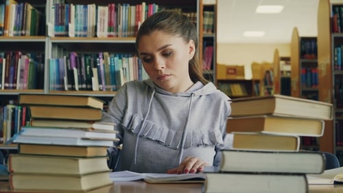 Concentrated Young Female Student Reading Books and Writing in Notebook During Working at School