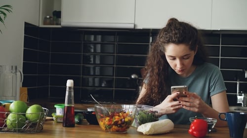 Woman Using Phone with Food Items in Kitchen
