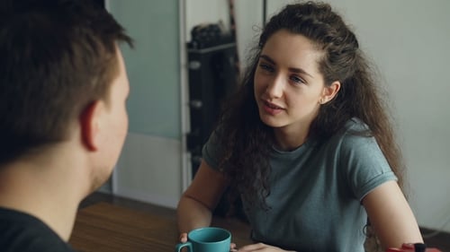 Young Caucasian Couple Sitting at Table in Modern Kitchen Dicussing Something in Positive Way
