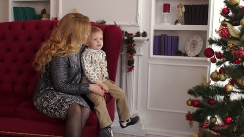 Mom and Son Sit on the Couch Near Christmas Tree