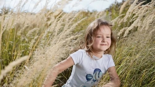 Sweet Baby-girl in a Beautiful Dress Running Across the Field of High-grass and Smiles Happily