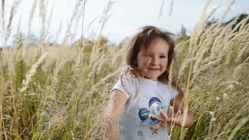 Encantadora y linda niña corriendo por la hierba alta y sonriendo alegremente, de humor juguetón, de buen humor