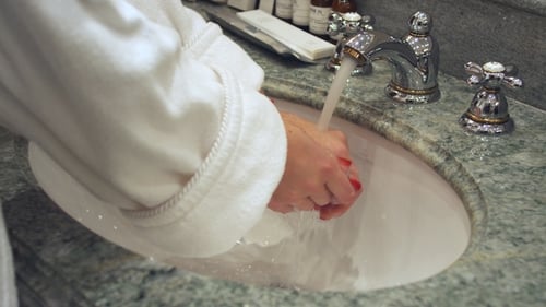 Woman Washing Hands at Marble Sink in Robe