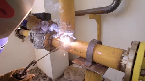Industrial Worker Wearing Protective Equipment Welding Metal Tubes on a Plant