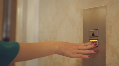 Female Hand Pushing Button for Calling Elevator in Apartment Corridor