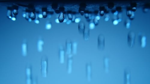 Dutzende von leuchtenden Klecksen fallen aus einer Duschdüse in einem blauen Badezimmer