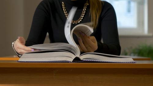 Women's Hands Leafing Through a Book. Woman Sitting at the Table Leafing Through the Book