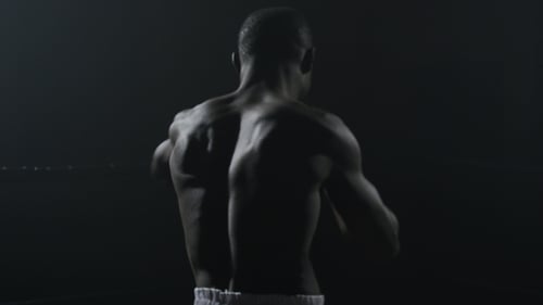 Rückansicht des muskulösen Mannes beim Boxen auf schwarzem Hintergrund. Afroamerikanischer junger männlicher Boxer beim Üben