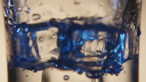 Ice Cubes in Glass and Water Pouring in It with Sparkling Bubbles in a Bar