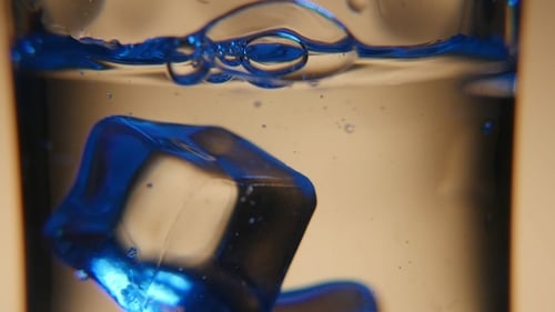 Five Cubes of Ice Are Thrown Into a See-through Glass with Fresh Water in Studio