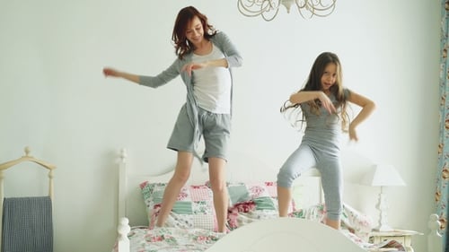 Funny Little Girl with Her Loving Mother Have Fun Dancing Modern Style Together Jumping on Bed