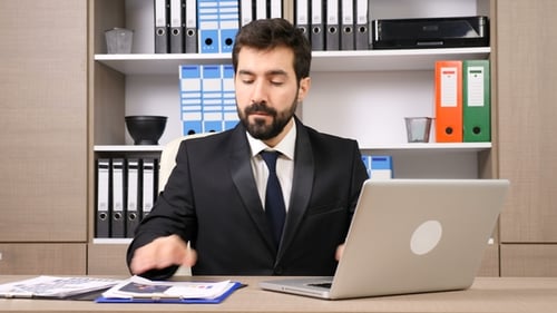 Man Working on Laptop and Documents in Office
