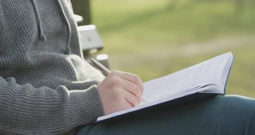 Person Writes in Notebook Outside on Sunny Day